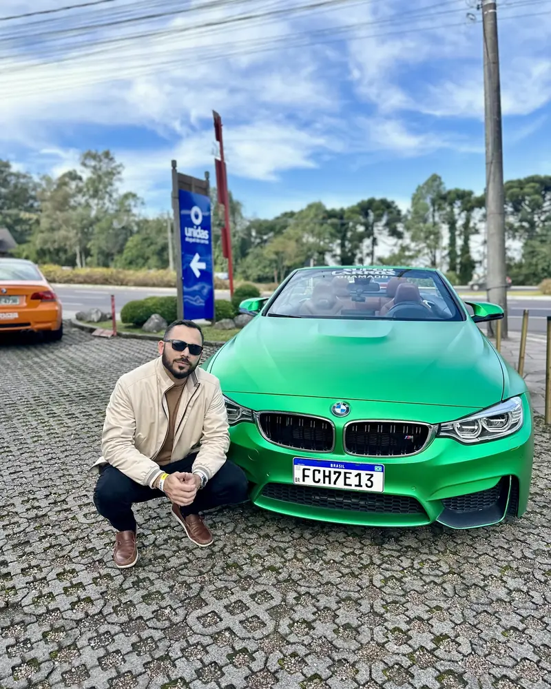 Alan agachado ao lado de um BMW verde