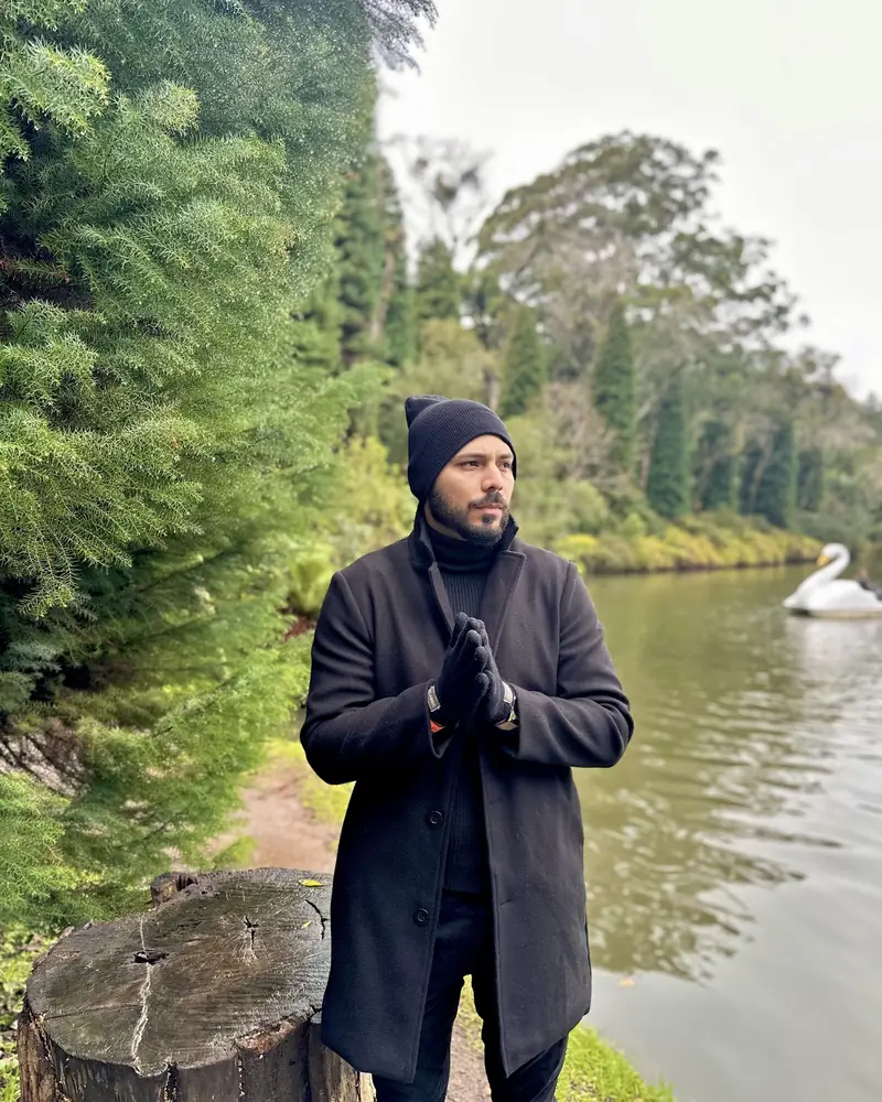 Alan de casaco preto à beira de um lago